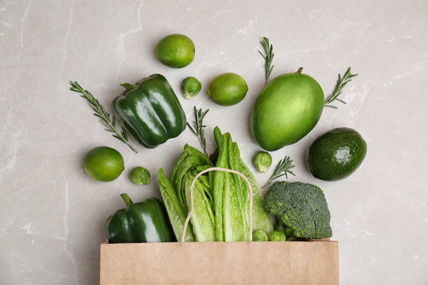 Paper package with green vegetables and fruits on grey background, top view - Valokuva, kuva