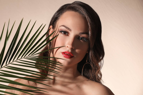 Portrait of young woman with beautiful professional makeup and palm leaf on light background - Photo, Image
