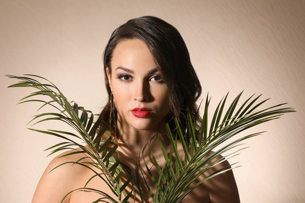 Retrato de mujer joven con hermoso maquillaje profesional y hojas de palma sobre fondo claro
 - Foto, imagen