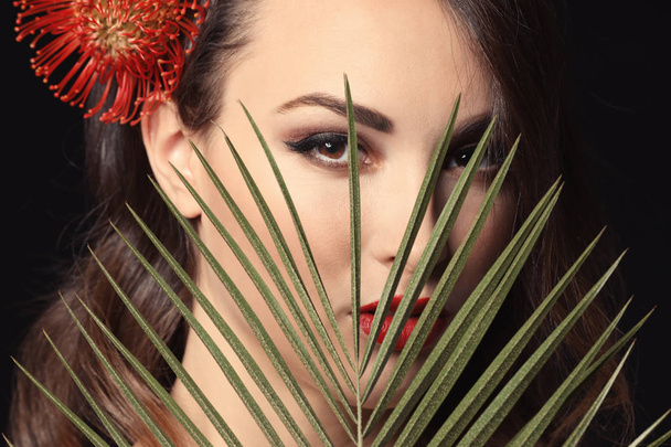 Portret van een jonge vrouw met mooie professionele make-up en palm blad op donkere achtergrond - Foto, afbeelding