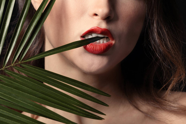 Sexy young woman with palm leaf on dark background, closeup - Foto, imagen