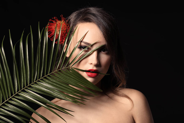 Портрет сексуальной молодой женщины с красивым профессиональным макияжем и пальмовым листком на темном фоне
 - Фото, изображение