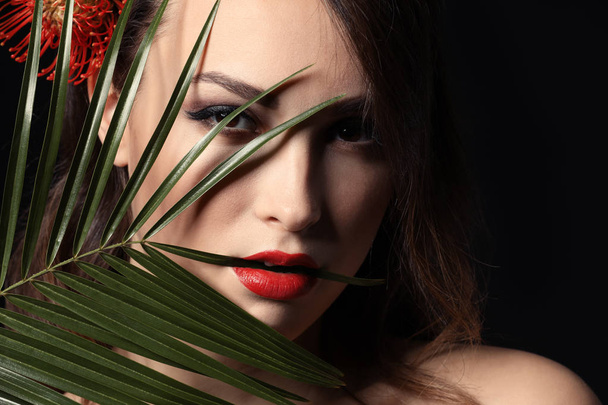 Portrait of sexy young woman with beautiful professional makeup and palm leaf on dark background - Zdjęcie, obraz