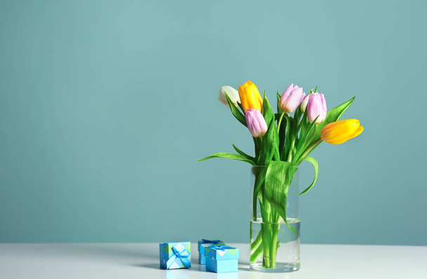 Vase with beautiful tulips and gift boxes on table against color background - Photo, Image