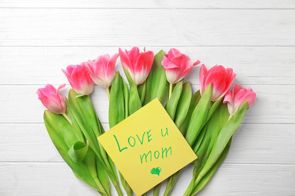 Hermosos tulipanes y tarjeta hecha a mano para el Día de la Madre sobre fondo de madera blanca, vista superior
 - Foto, Imagen