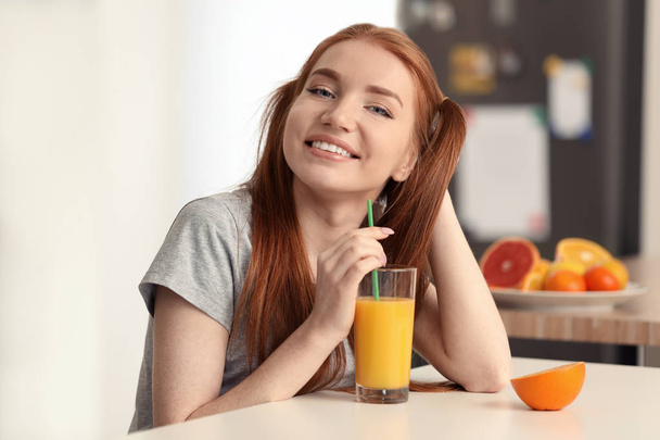 Beautiful young woman drinking citrus juice in kitchen - Photo, Image