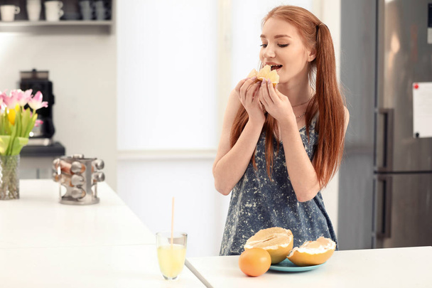 Beautiful young woman eating citrus fruit in kitchen - Photo, Image