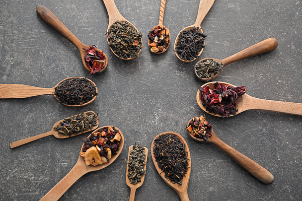 Lepels met verschillende soorten droge thee bladeren op grijze achtergrond - Foto, afbeelding