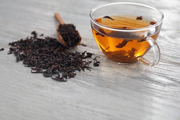 Dry black tea leaves and cup of aromatic beverage on table - Photo, Image