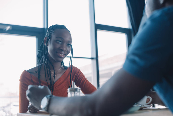 smiling african american woman looking at boyfriend in coffee shop - Foto, imagen