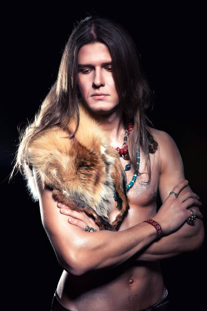 a young man with long hair and a fur coat on his naked body - Фото, изображение