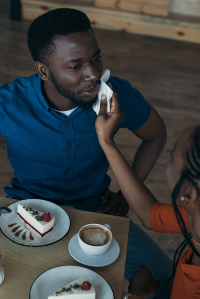 high angle view of careful african american woman cleaning boyfriends face with napkin at table in cafe - Photo, Image