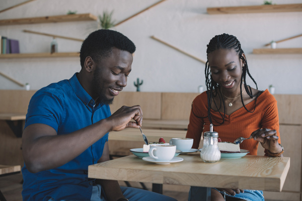 smiling african american couple at table with cups of coffee and desserts in cafe - Photo, Image