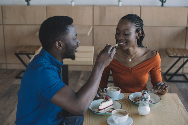 african american man feeding girlfriend with dessert on romantic date in cafe - Photo, Image