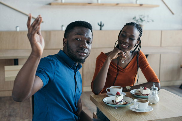 コーヒーとカフェでデザートのカップをテーブルに座っているアフリカ系アメリカ人のカップル - 写真・画像