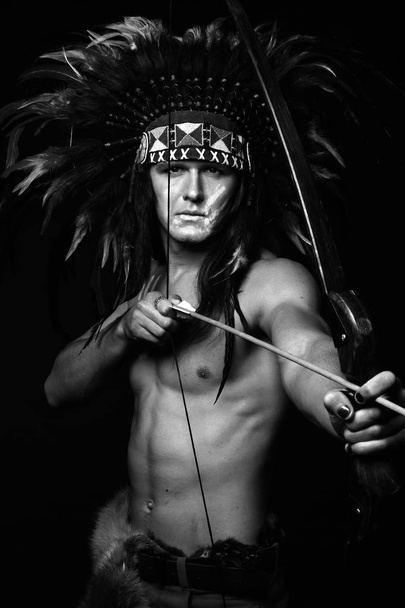 a young man in a headdress of Indians of blue feathers with a bow in his hands - Fotografie, Obrázek