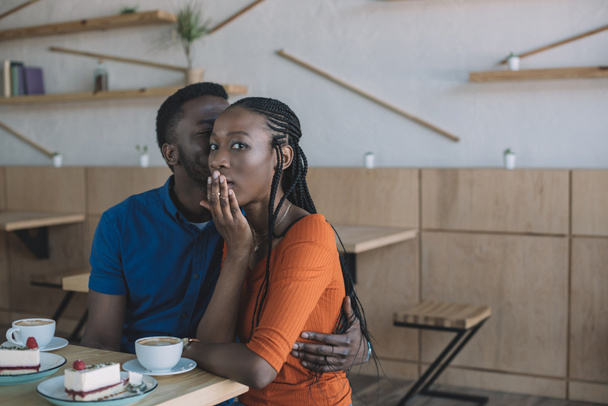 african american man telling secret to shocked girlfriend at table in cafe - Фото, зображення