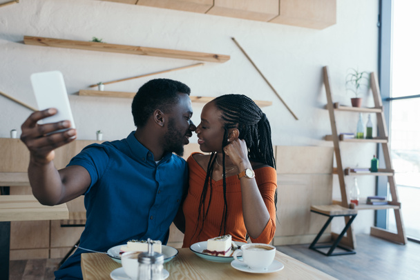 Afrika kökenli Amerikalı çift alarak selfie smartphone cep telefonu ile kahve dükkanında birlikte seçici odak - Fotoğraf, Görsel