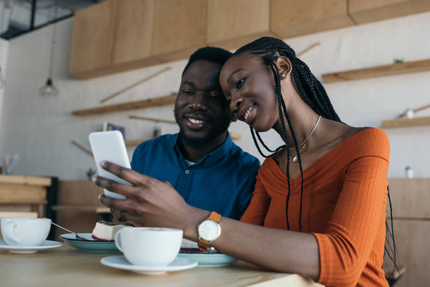 cheerful african american couple using smartphone together in coffee shop - Fotografie, Obrázek