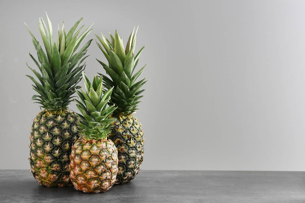 Fresh ripe pineapples on table against grey background - Foto, afbeelding