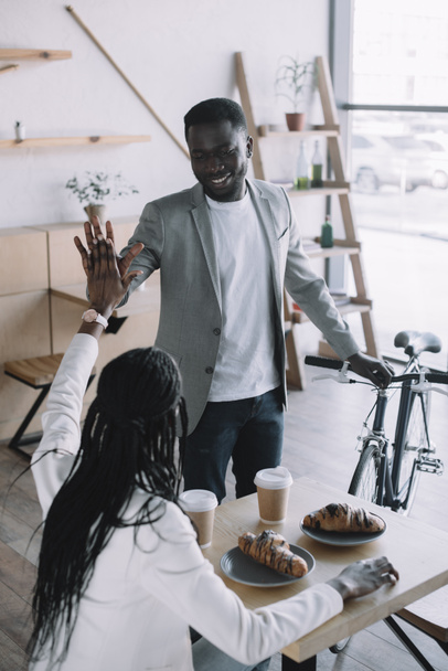 african american friends giving high five to each other at table in cafe - Photo, image