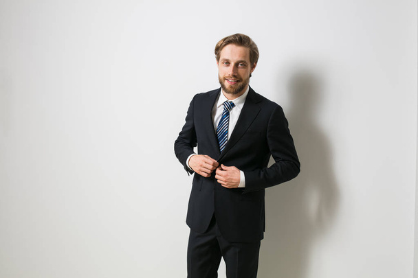 blonde guy with a beard in an elegant suit, closing his coat, looking confidently and smiling at the camera, successful businessman - Foto, Imagem