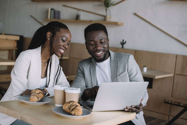 muotokuva hymyilevä afrikkalainen amerikkalainen ystävät käyttävät kannettavaa tietokonetta yhdessä pöydässä kahvilassa
 - Valokuva, kuva