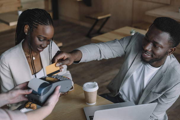 Afrikanisch-amerikanischer Mann bezahlt Bestellung mit Kreditkarte, während er Zeit mit Freund im Café verbringt - Foto, Bild