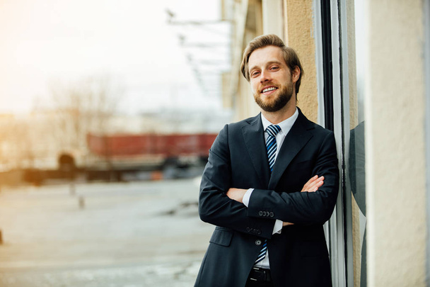 elegant blonde man in costume, mature with beard,leaning against a building, looking with confidence and smiling to camera - Photo, Image