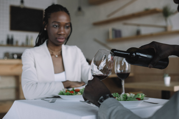 częściowy widok african american nalewania wina do kieliszka, podczas romantyczną randkę z dziewczyną w restauracji - Zdjęcie, obraz