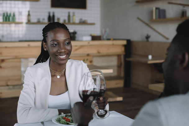 partial view of african american couple clinking glasses of wine in restaurant - Foto, imagen