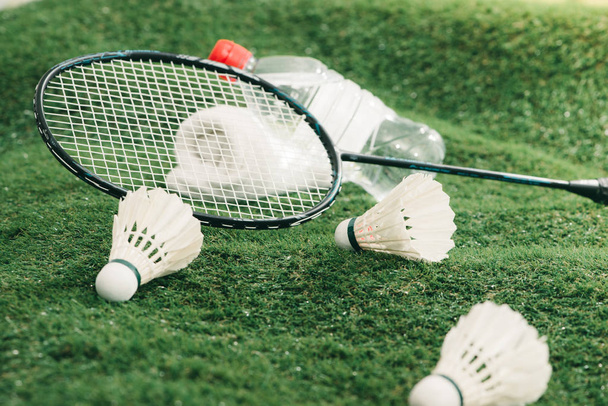 Shuttlecock and badminton rackets, towel and bottle of water on green grass - Photo, image