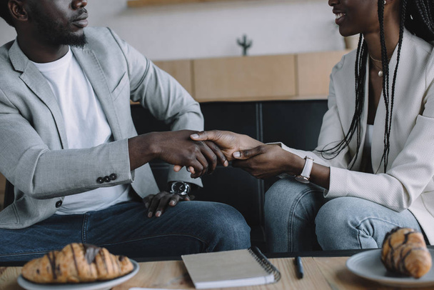gedeeltelijke weergave van Afro-Amerikaanse business partners handen schudden tijdens zakelijke bijeenkomst in café - Foto, afbeelding