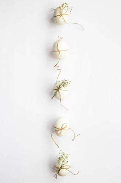 White minimalistic Easter eggs decorated with twine and flowers of gypsophila on a white background lined with a line. Easter concept. Top view, flat lay - Φωτογραφία, εικόνα