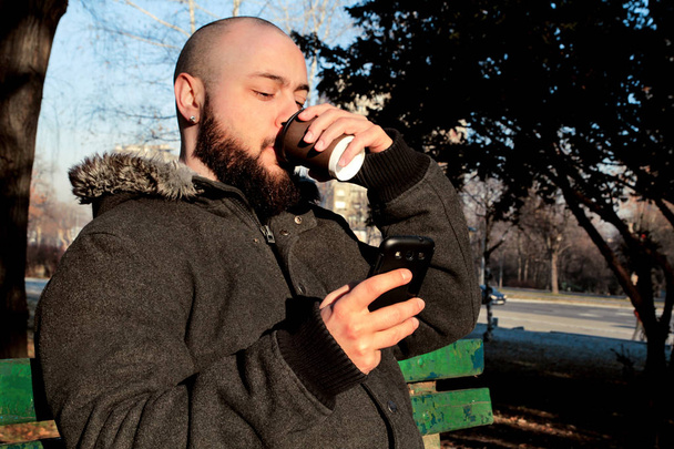 Az ember ül a parkban a smartphone és elvihető kávéfogyasztás - Fotó, kép