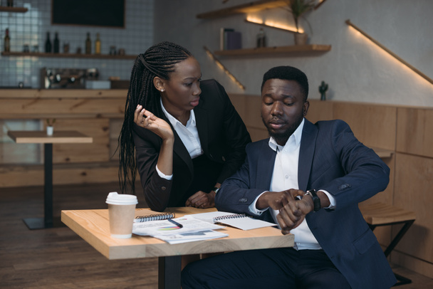 Африканский американский бизнесмен проверяет время с коллегой на встрече в кафе
 - Фото, изображение