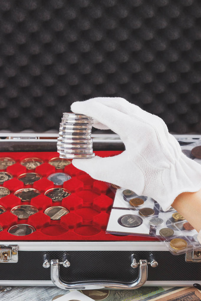 Рука в белой перчатке держит коробки с коллекционными монетами
 - Фото, изображение