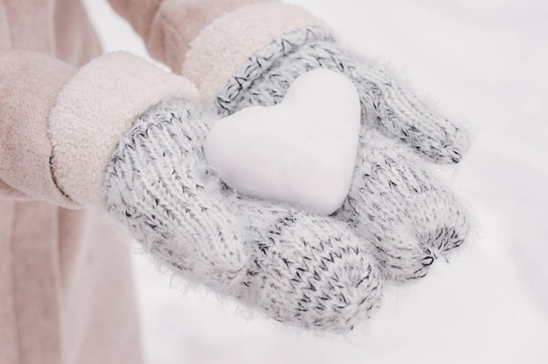 Ręce w wełniane rękawice trzymając piłkę śniegu w kształcie serca. Zimowy nastrój. Symbol miłości - Zdjęcie, obraz
