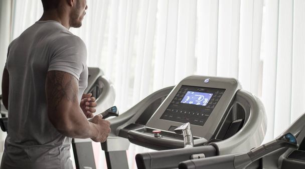 Muscular builder man running in machine treadmill at fitness gym club - Photo, image