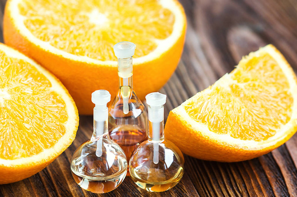 木製の背景に、熟したジューシーな新鮮なオレンジ色のフルーツのガラス瓶の中の本質的なアロマオイル。美容トリートメント。スパのコンセプトです。選択と集中。木製のテーブルの水平方向のオレンジ マクロの香りのオイル - 写真・画像