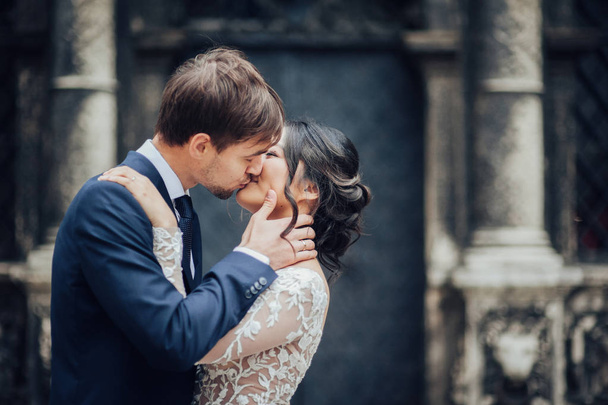 Groom and bride kissing with blurred old building on background - Foto, afbeelding