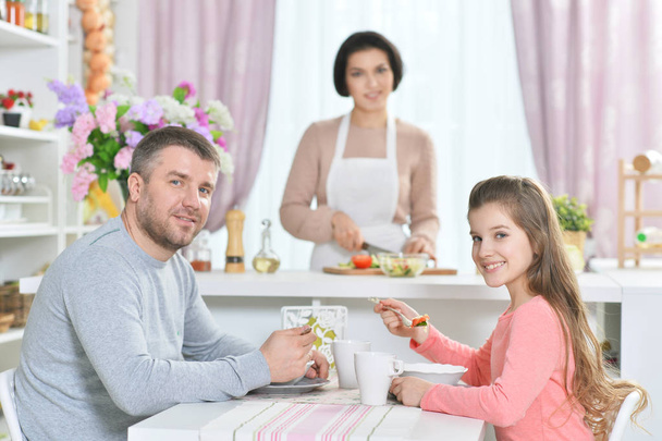 smiling girl and  father eating  at kitchen with mother  on background - Foto, Bild