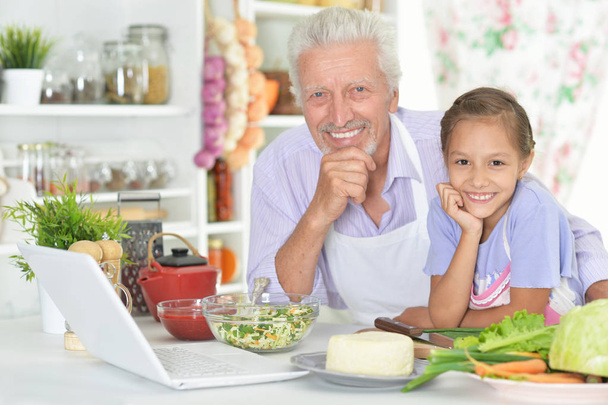 Senior man with granddaughter preparing dinner in kitchen - Фото, изображение