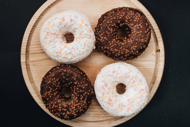 сладкие домашние пончики с сахарной крошкой и шоколадной глазурью на деревянной доске
  - Фото, изображение