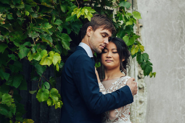 Bride with groom tenderly posing in green branches - Foto, Bild