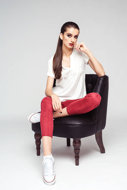 full length fashion portrait of attractive brunette woman in stylish clothes posing sitting on arm-chair - Foto, Imagem