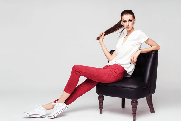 full length fashion portrait of attractive brunette woman in stylish clothes posing sitting on arm-chair - Valokuva, kuva