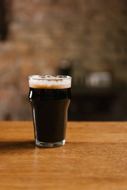 fresh cold dark beer with foam in glass on wooden table in pub - Foto, Imagem