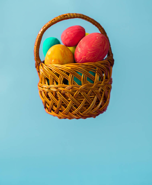 Easter eggs in a wicker basket on a blue background - Φωτογραφία, εικόνα