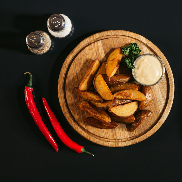 смачна запечена картопля з соусом на дерев'яній дошці, спеціями та перець чилі на чорному
  - Фото, зображення